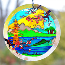 Hanging stained glass suncatcher with a golden Buddhist temple on a blue lake against Japanese mountains with cherry blossom