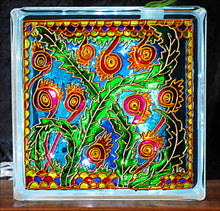 A stained glass block suncatcher or night light, hand painted with snake like flowers and green leaves against a blue sky