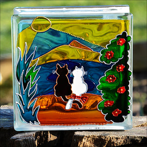 A colourful stained glass suncatcher block by Ornately Lanterns with a cat couple on a golden beach in front of a blue sea