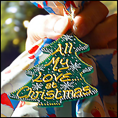 A hand holds a festive present and its green Christmas tree gift tag, personalised with the message “All my love at Christmas”