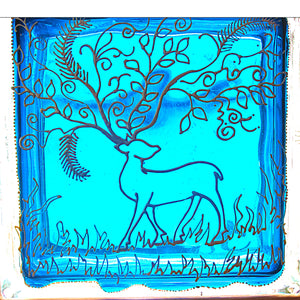 A stained glass block window decoration painted in bright blue and patterned with a silver reindeer and his lacy floral antlers
