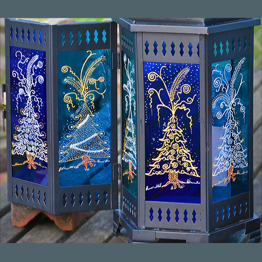 Holiday window decoration ideas, a Moroccan style candle lamp with gold & silver Christmas trees on blue stained glass panels