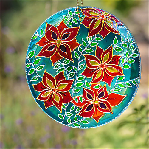 Stained glass circle suncatcher with large clematis flowers in red, pink & gold trailing across a blue & turquoise background