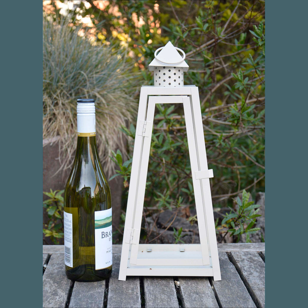 A shabby chic garden lantern with a cream frame standing next to a wine bottle – it’s a little taller than the bottle