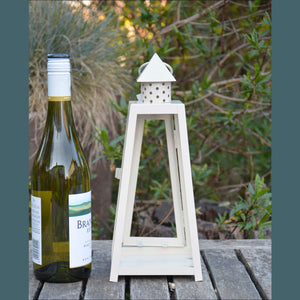 A shabby chic garden lantern with a cream frame standing next to a wine bottle – it’s the same height as the bottle