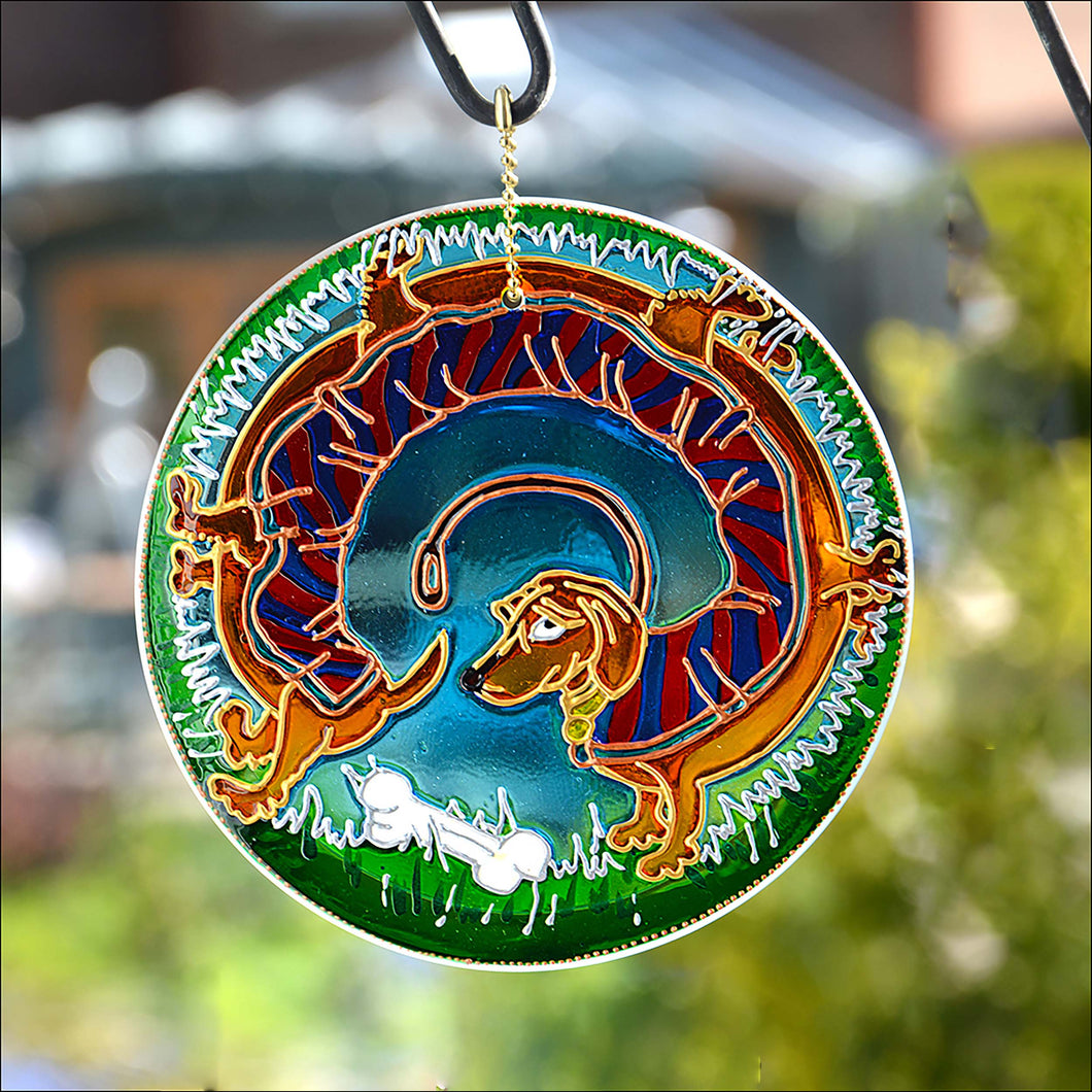 A hanging stained glass circle hand painted with a colourful dachshund dog who stretches all the way around the suncatcher