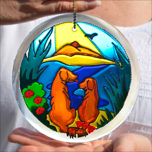 A hanging stained glass suncatcher original, hand painted with a seaside scene featuring a loving Golden Retriever dog couple