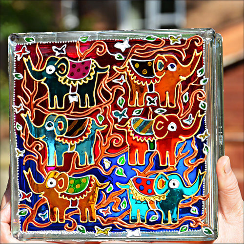 A square stained glass block suncatcher in brilliant rich colour, hand painted with six happy raised trunk elephants