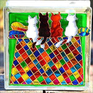 A square stained glass block suncatcher by Ornately Lantern, hand painted with four happy cats sitting on a colourful carpet