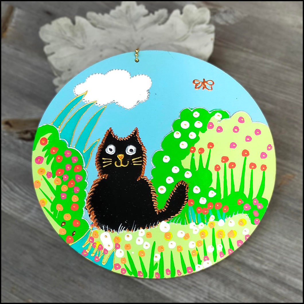 Plywood circle wall hanging hand painted in bright cheerful colours; fluffy black cat in garden with flowers; cat lover gift
