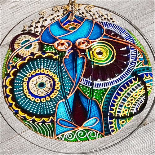 A glass circle suncatcher patterned with an intricate hand painted mandala design in blue, green, turquoise, gold & silver