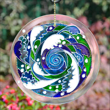 A stained glass suncatcher painted with an Oriental style whirlpool in blues and greens