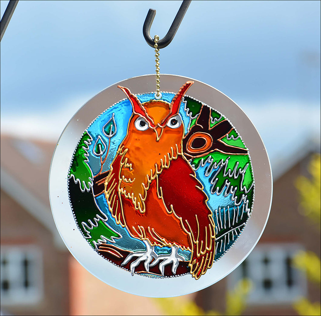 A hanging stained glass suncatcher, hand painted with a woodland theme – a large red gold and orange owl perches on a branch 