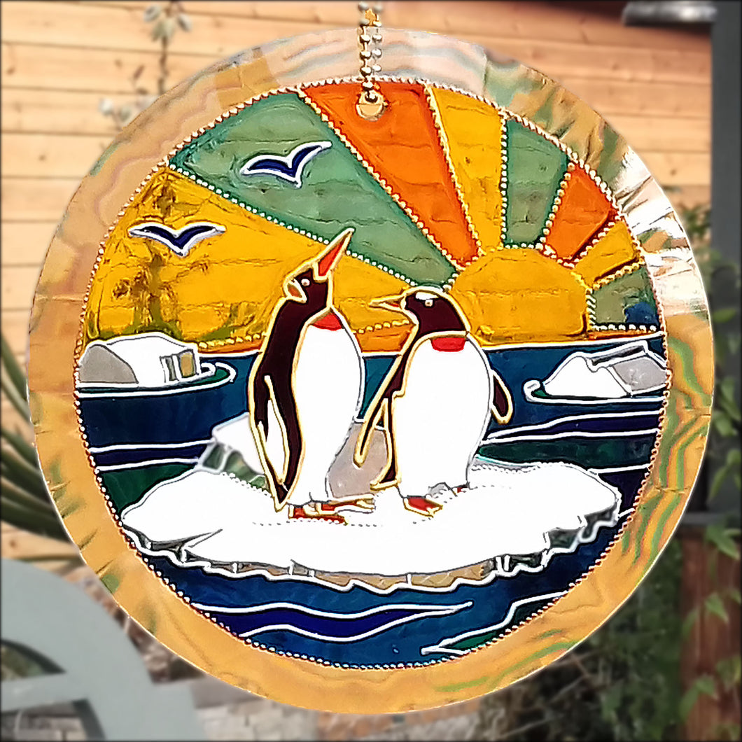 A glowing stained glass suncatcher with two penguins in the snow on an ice cap in the ocean & the sun rising behind them