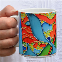 A hand holds a bright and cheerful abstract art patterned coffee mug – white, blue, red, green, gold, silver, pink, orange