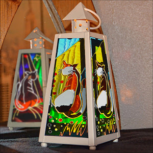 A shabby chic cream tealight lantern sits opposite a mirror so 3 glass panels show – a hand painted cat in sunshine on each