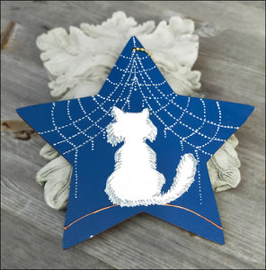 A lightweight wooden star wall hanging, richly blue with a hand painted glossy white cat and web of silver snowflakes on top