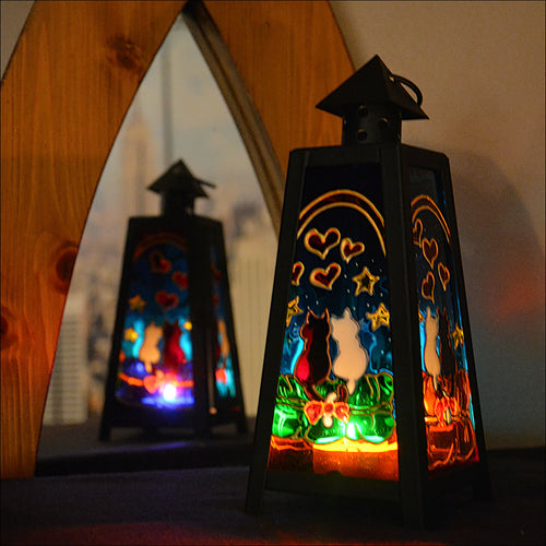 A candle burns in a tealight lantern opposite a mirror, 3 glass panels show a cute cat couple with stars & hearts on each one