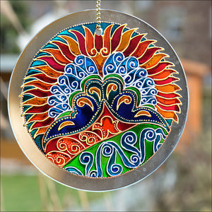A 6” glass circle suncatcher hand painted in warm sunset colours & an Art Deco “peacock” theme design