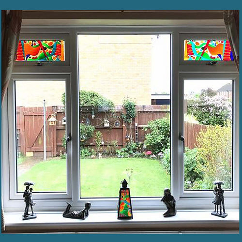 Clear glass windows look out onto a garden and two small stained glass window panels glow in the light