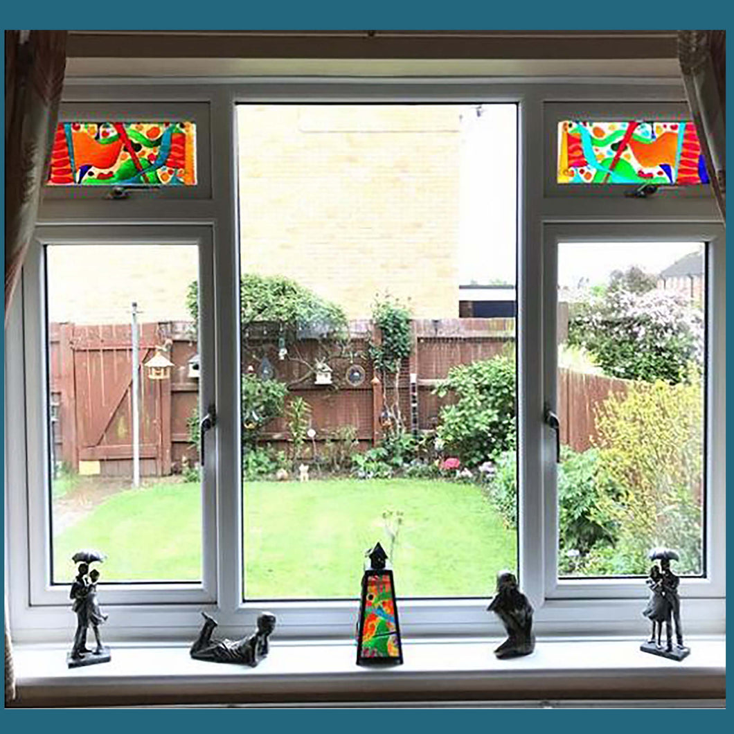Clear glass windows look out onto a garden and two small stained glass window panels glow in the light